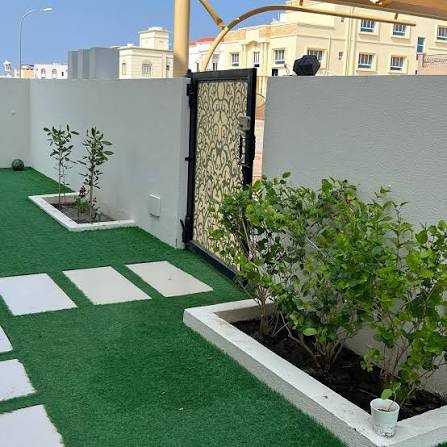 فناء جانبي بثيل صناعي وبلاط ممرات وأحواض نباتات بيضاء وبوابة مزخرفة